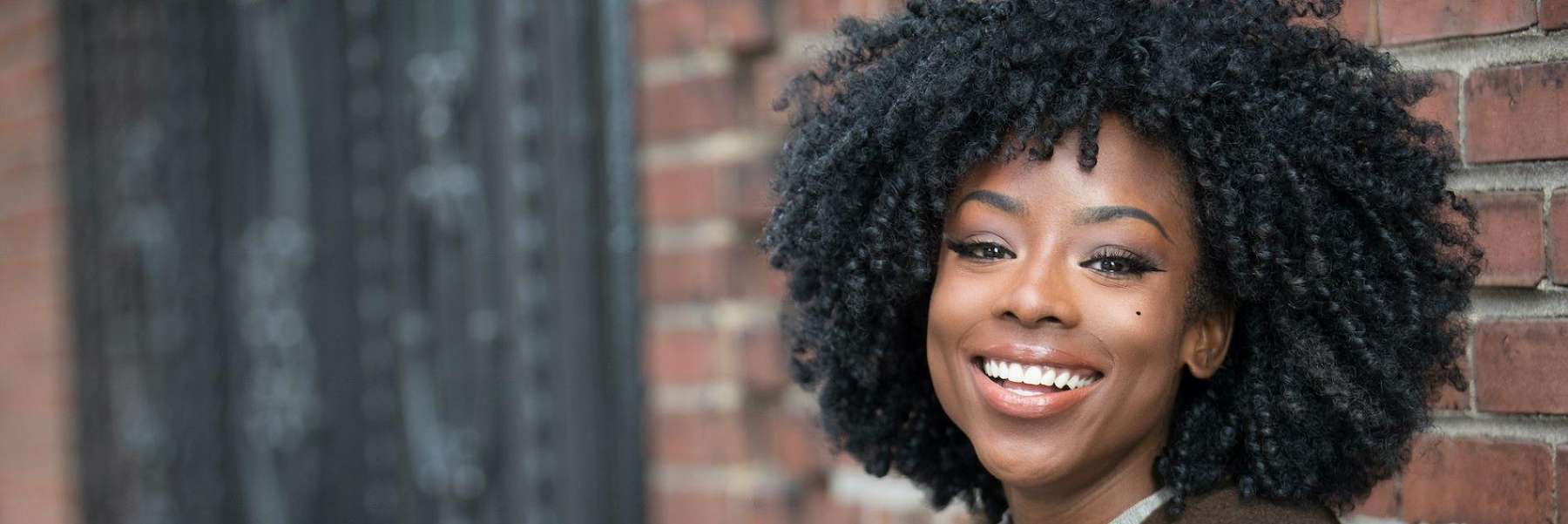 A woman smiling against a brick wall
