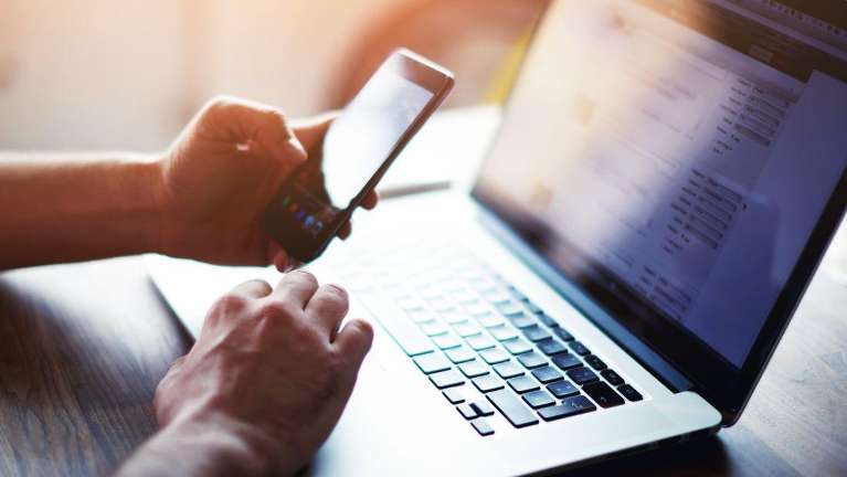 A person working on their cell phone and laptop
